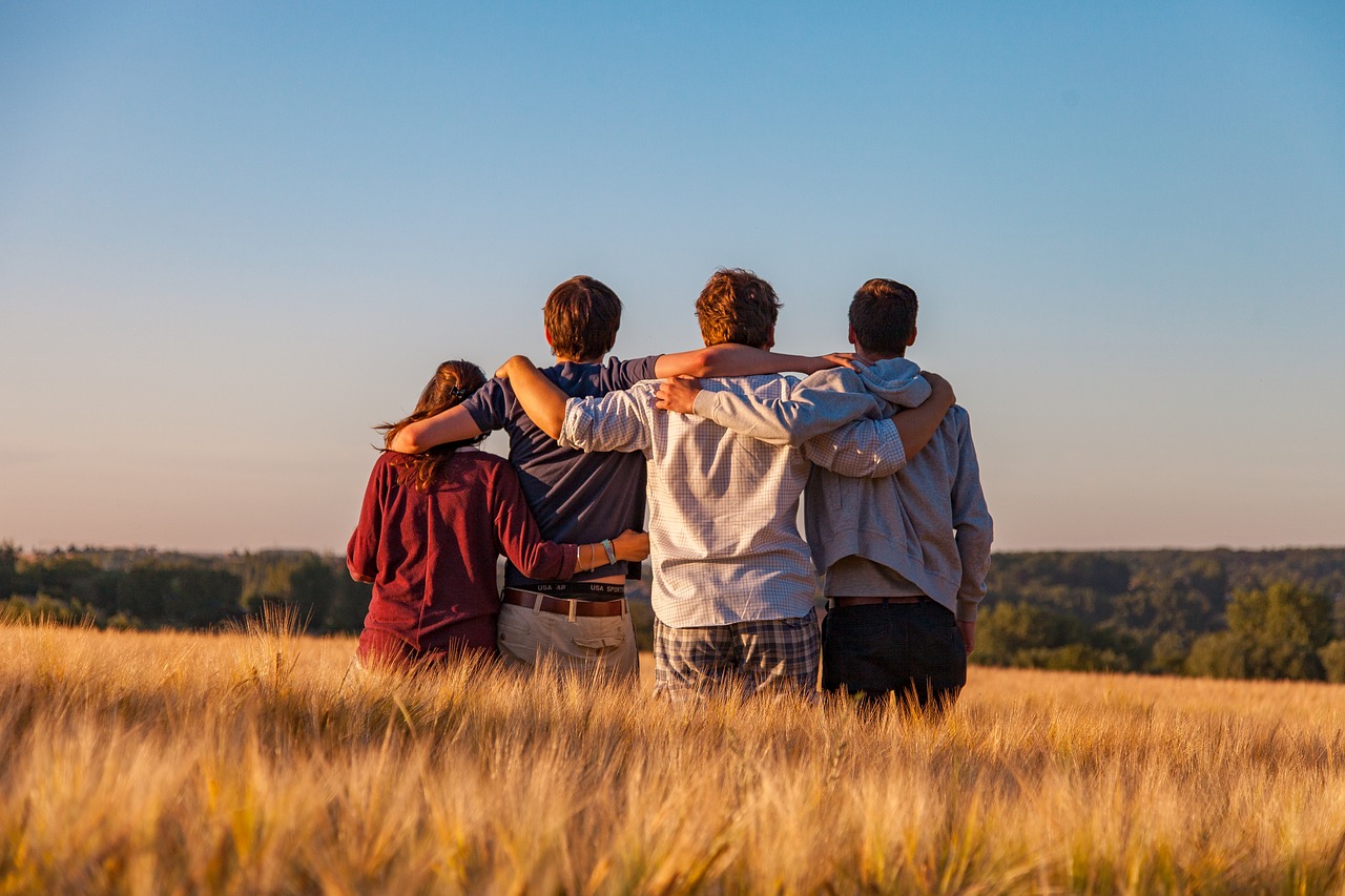 négy fiatal háttal áll és néz előre néz egy mezőn