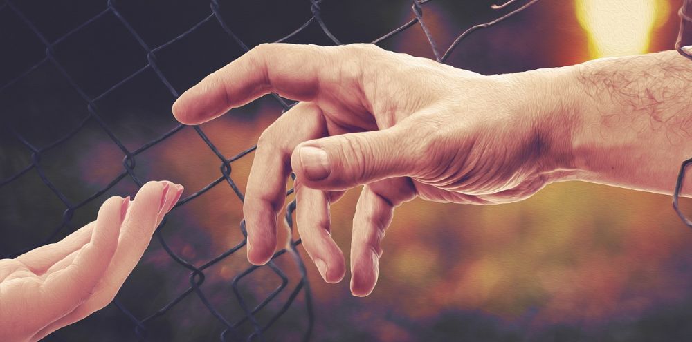 Két kéz egymáshoz ér a kerítésen keresztül