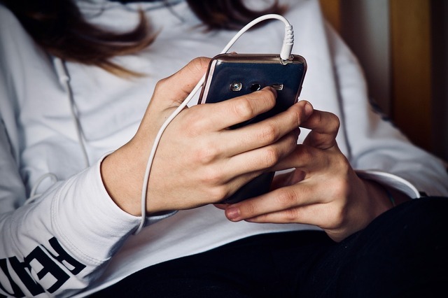 A fotó részlet egy mobilt a kezében tartó fiatal nőt ábrázol