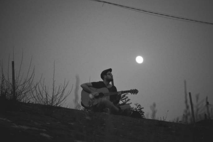 Fekete-fehér fotó Havas Ádámról, gitározás közben 